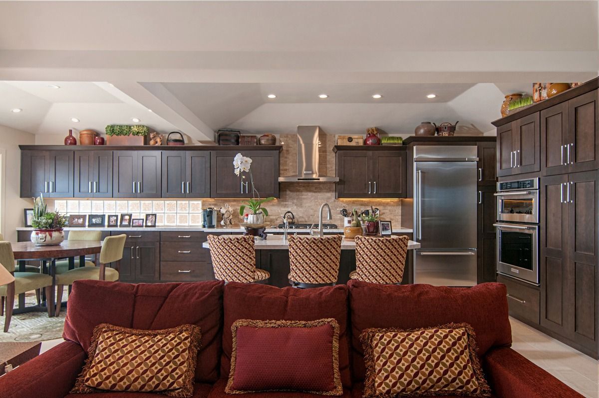 Burgundy sofa facing a dark wood kitchen with a stainless steel refrigerator and oven. A dining table is visible to the left.