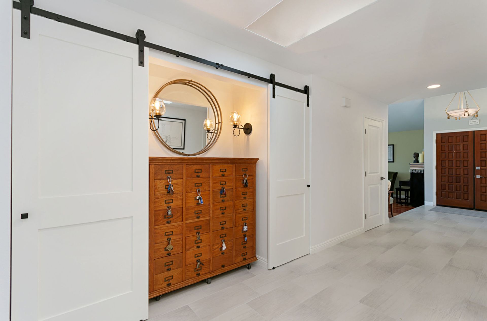 Barn doors slide open to reveal a wooden chest with a mirror and sconces, located in a hallway.
