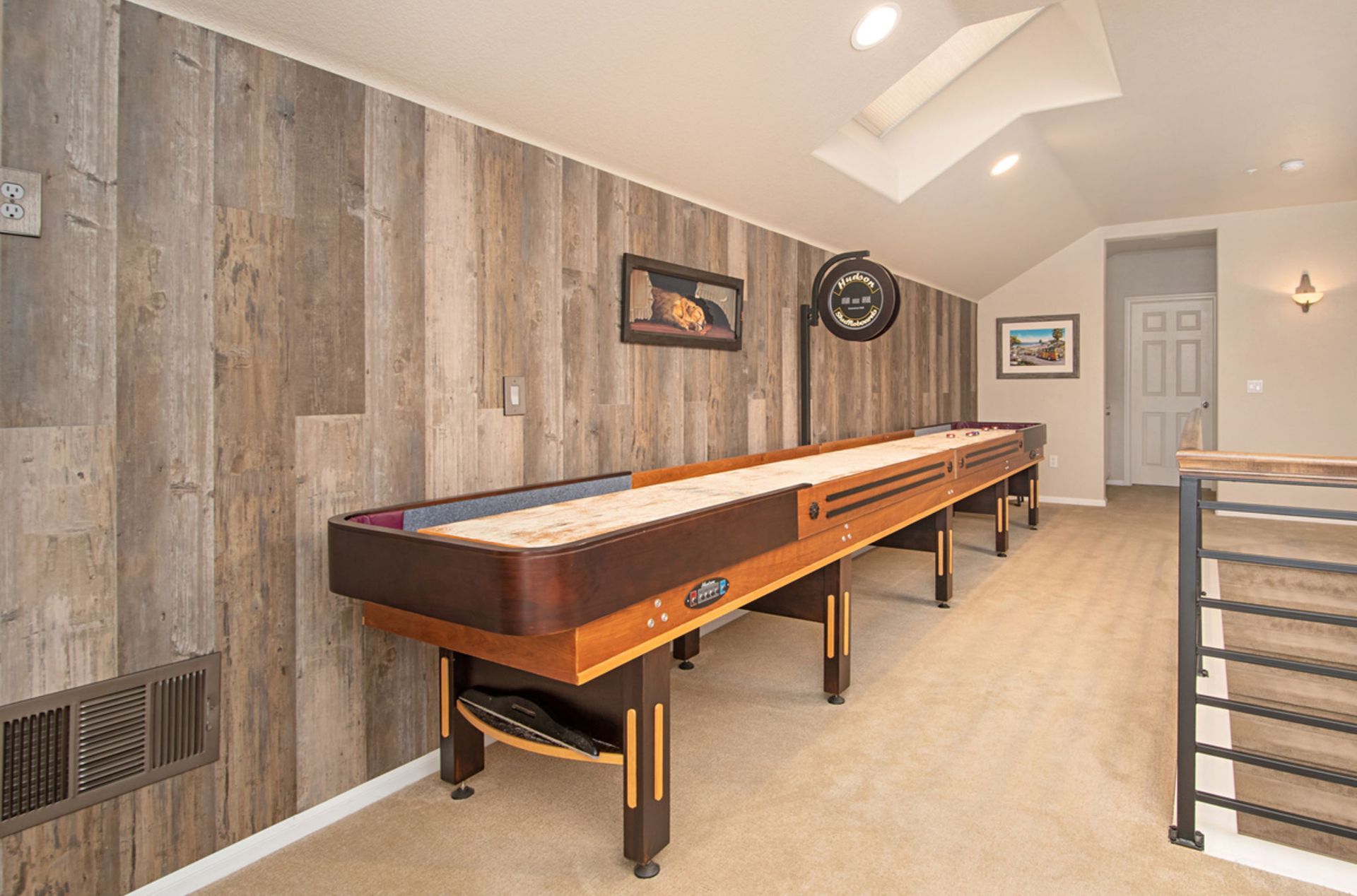 Shuffleboard table in a room with wood paneling, a skylight, and carpeted floor. A door and metal railing are also visible.