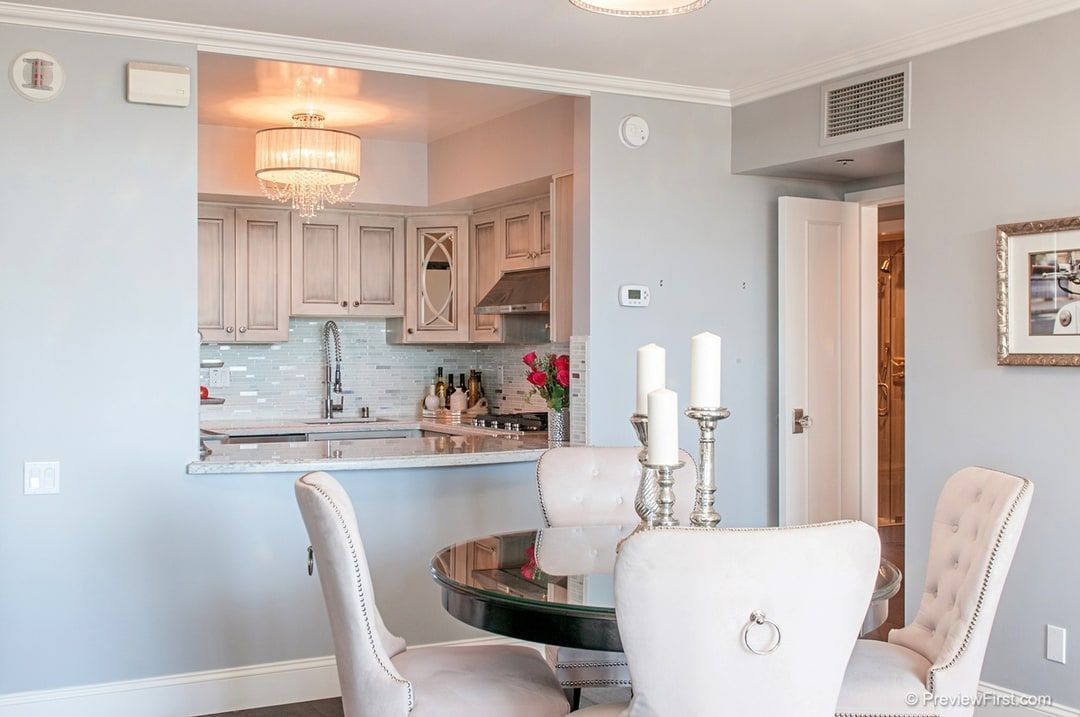Dining area with round table and upholstered chairs, open to a kitchen with light-colored cabinets.