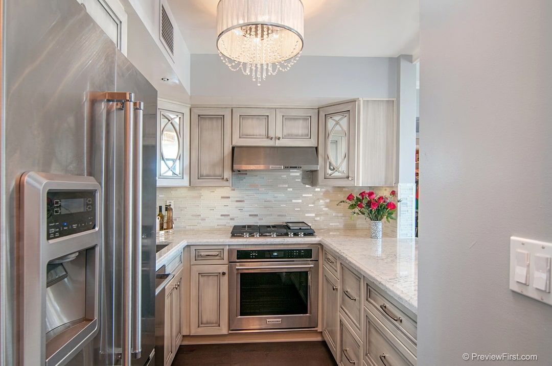 U-shaped kitchen with stainless steel appliances and off-white cabinets, marble countertops, and a chandelier.