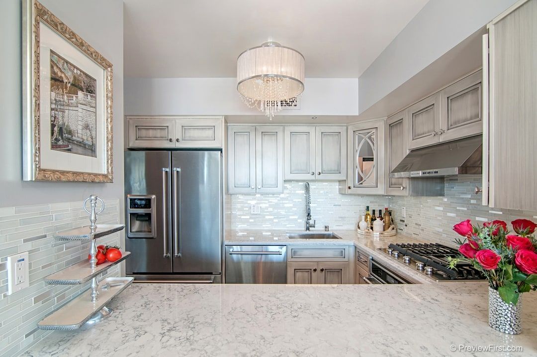 Bright, airy kitchen with stainless steel appliances, light gray cabinetry, and a granite countertop. A chandelier hangs above the sink.
