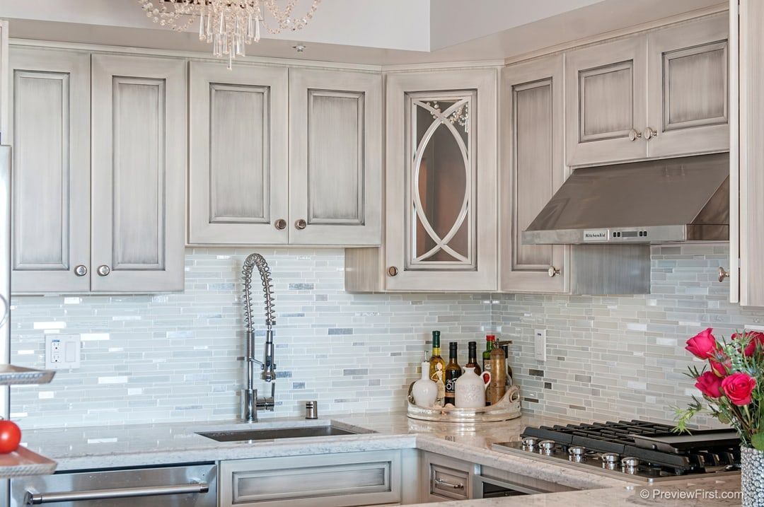White kitchen cabinets with a decorative glass door above a sink and tiled backsplash.