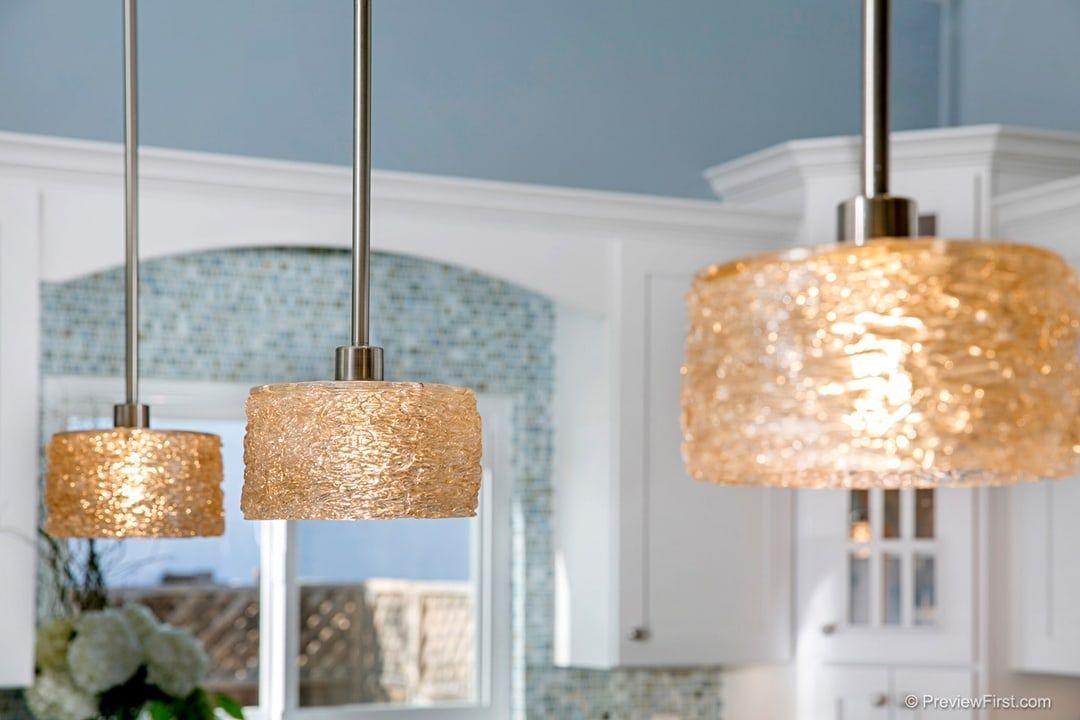 Three pendant lights with textured gold shades hang in a kitchen with white cabinets and a blue wall.