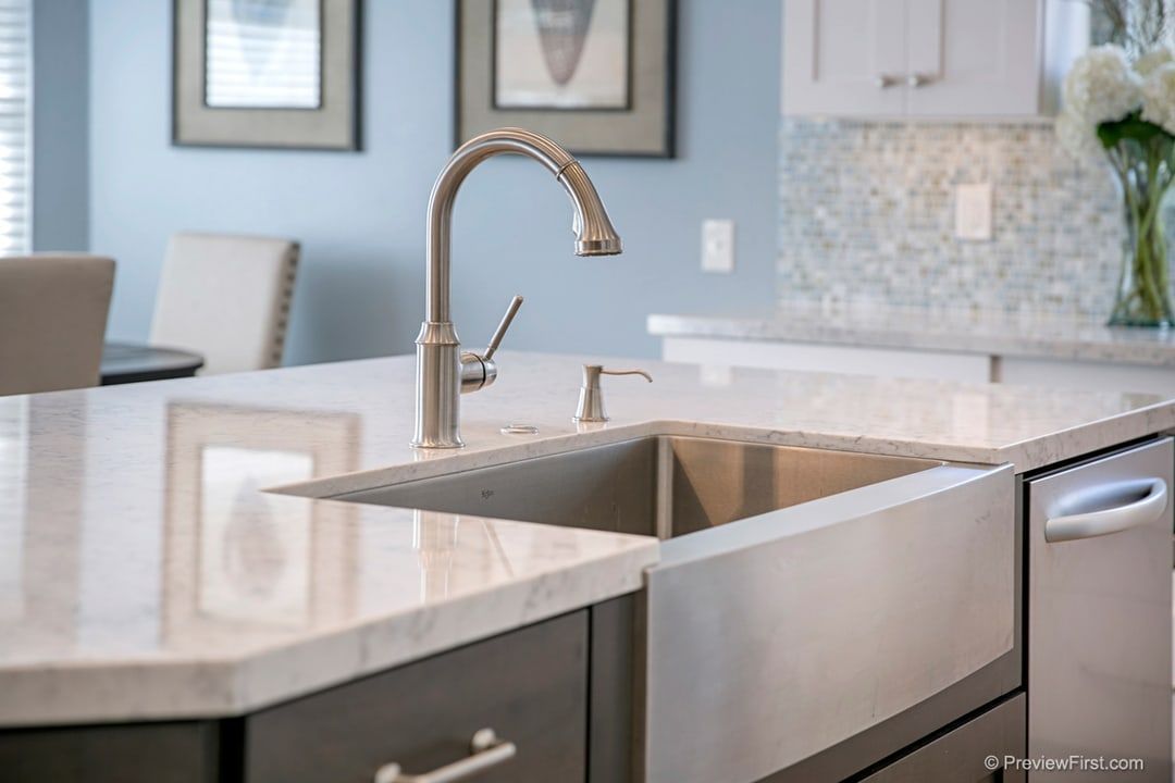 Stainless steel farmhouse sink in a modern kitchen island with a white countertop, faucet, and soap dispenser.