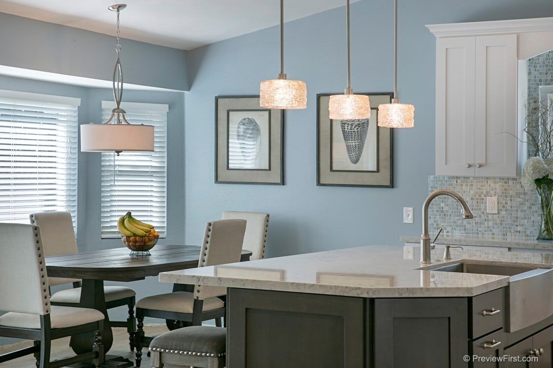 Kitchen with blue walls, a dark island, and a round table. Hanging lights illuminate the space, and framed art adorns the wall.