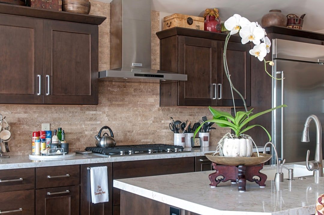 A modern kitchen with dark brown cabinets, stainless steel appliances, and a white orchid in the foreground.