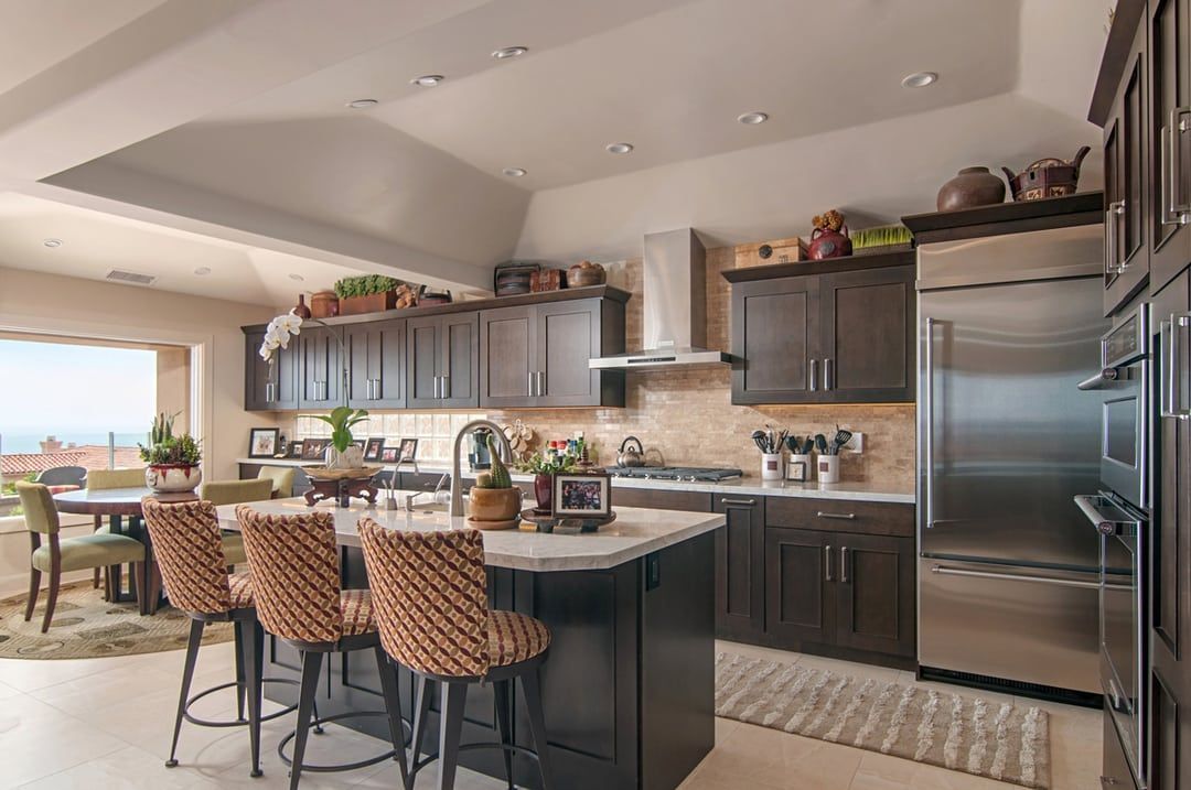 A modern kitchen with dark brown cabinets, a stainless steel refrigerator, and a kitchen island with woven bar stools.