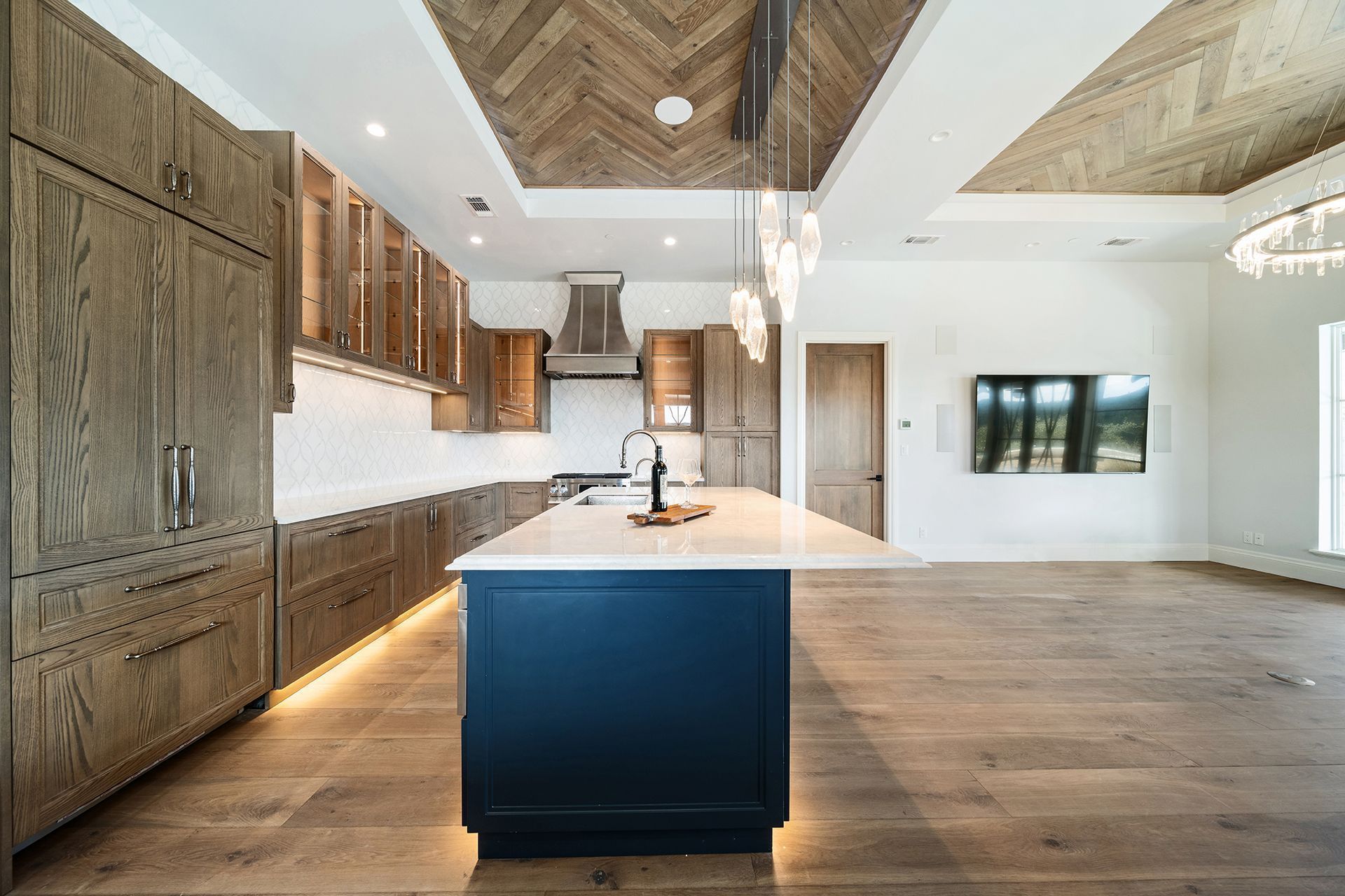 A modern kitchen featuring wooden cabinets, a blue island with a white countertop, and a herringbone wood ceiling.