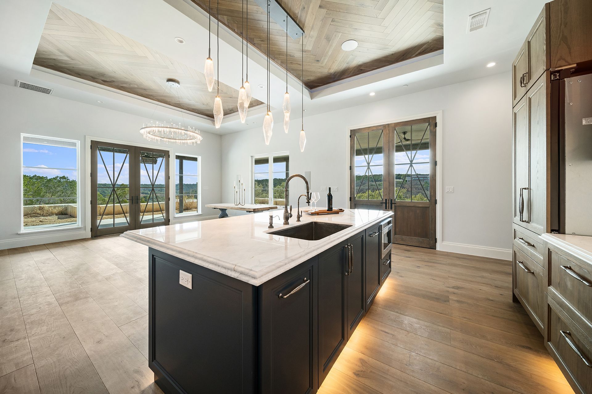 Spacious kitchen with a large island, hardwood floors, and windows overlooking a scenic outdoor view. Dark cabinets and a light countertop.
