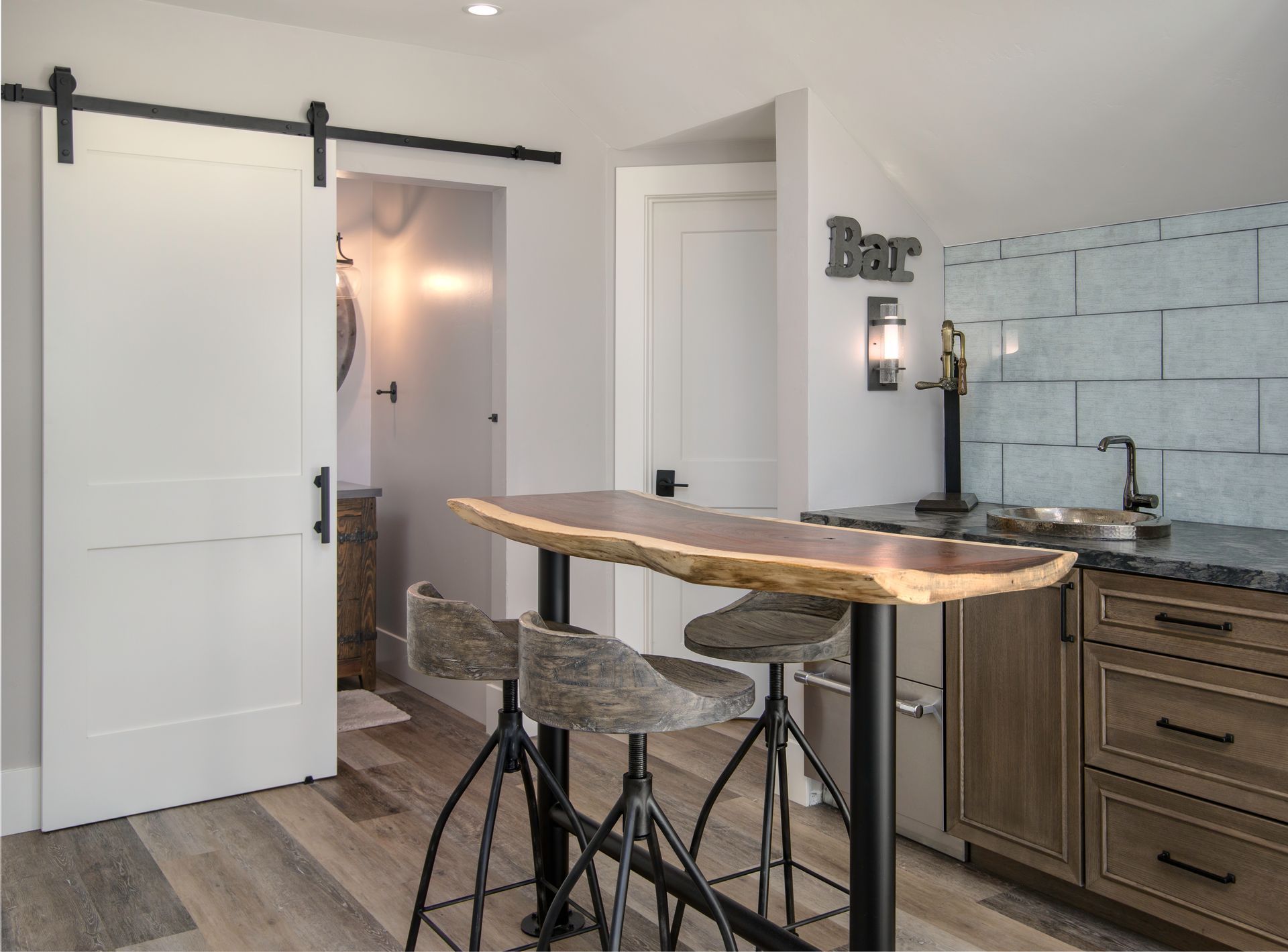 A home bar with a wooden countertop, stools, and a sliding barn door leading to a bathroom.