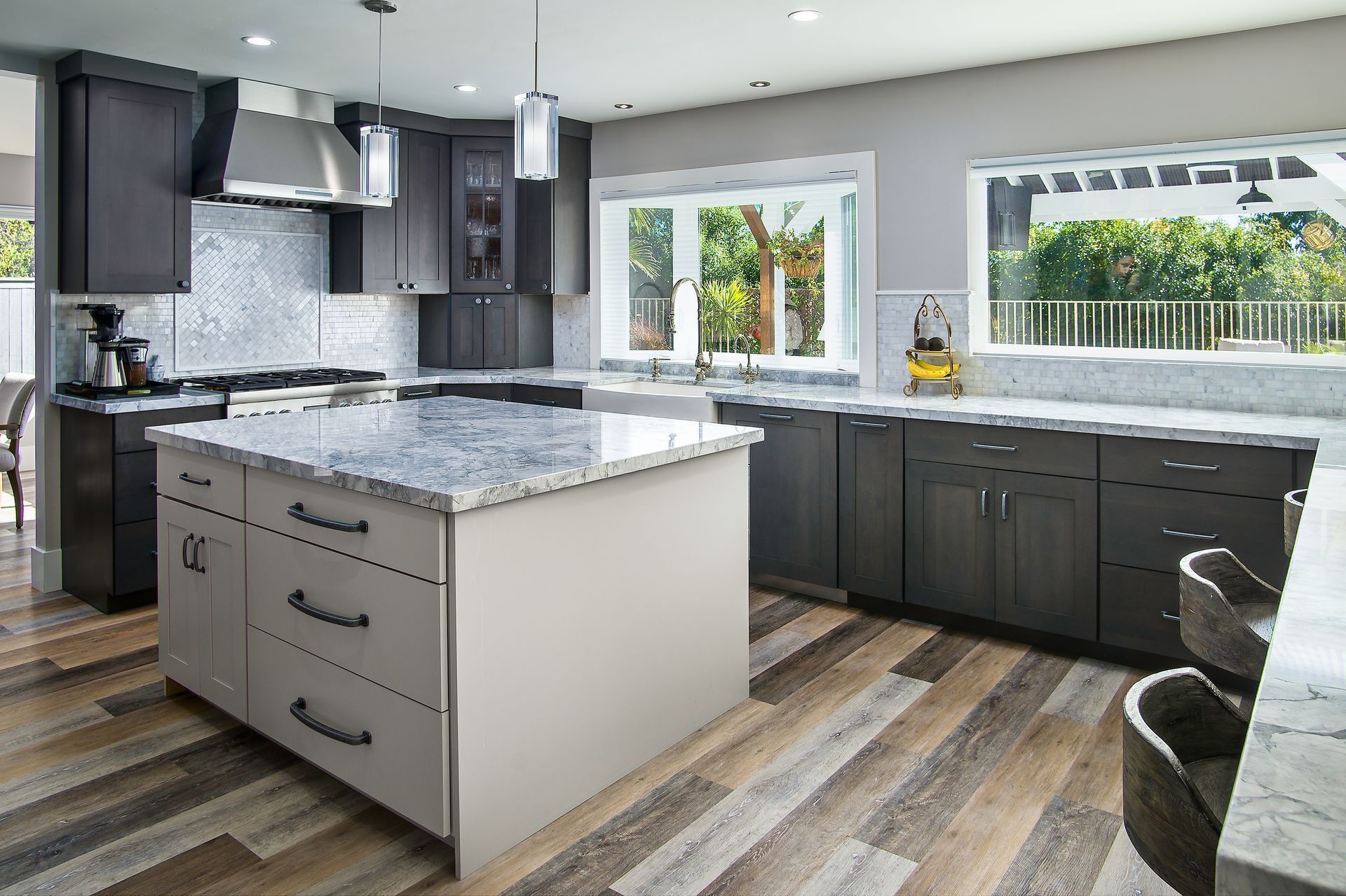 Modern kitchen with a gray island, dark gray cabinets, light wood floor, and a large window overlooking a yard.