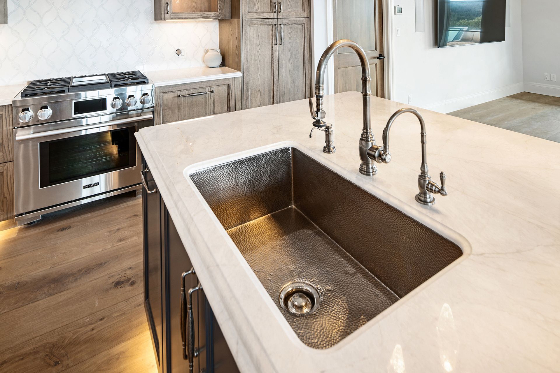 A kitchen island with a copper sink and two faucets. A stainless steel oven and cabinetry are in the background.