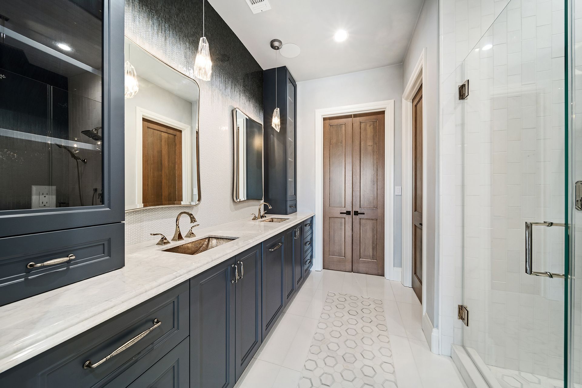 Long, narrow bathroom with dark blue cabinets, two mirrors, and a glass shower.