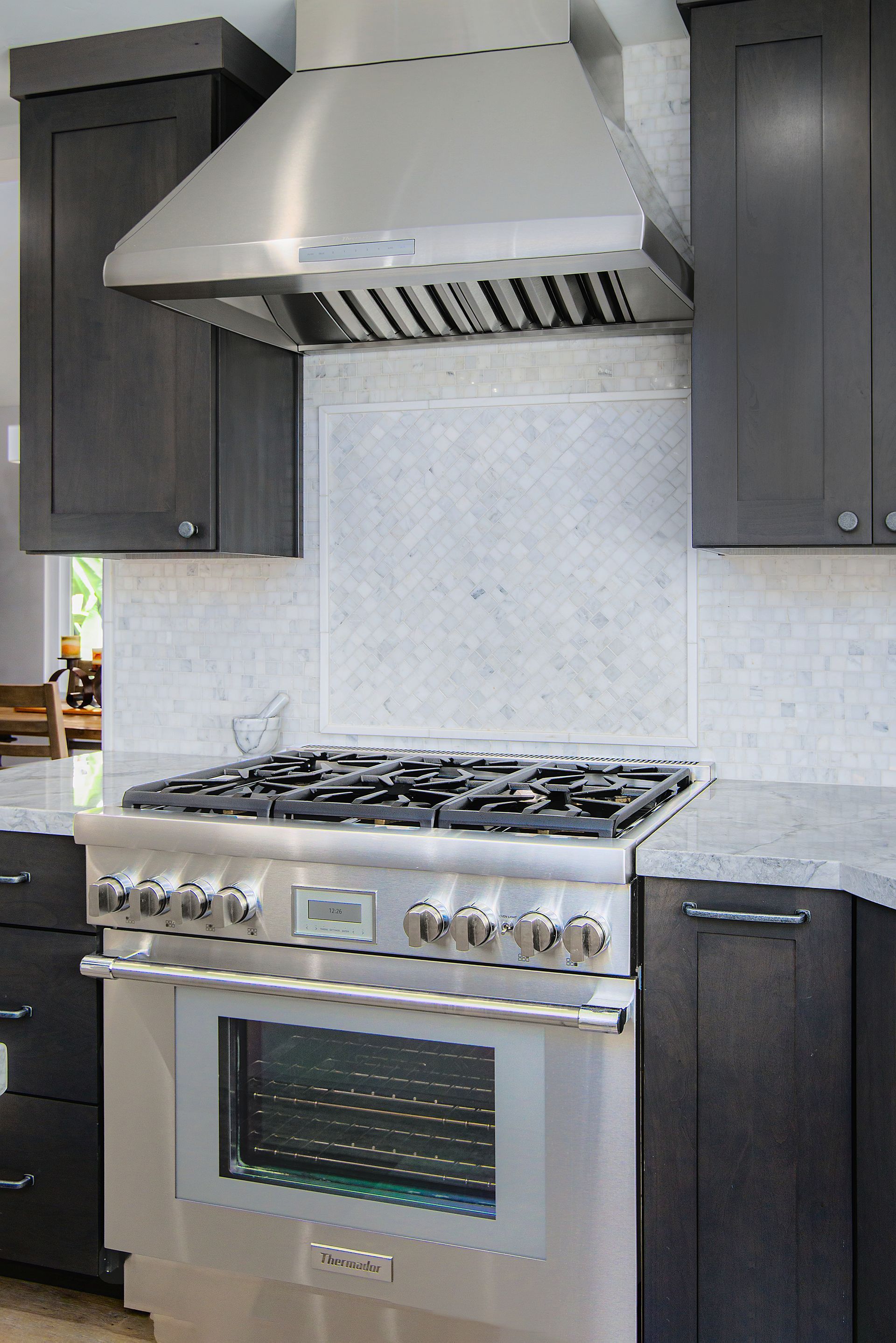Stainless steel range and hood in a modern kitchen with dark gray cabinets and white tile backsplash.