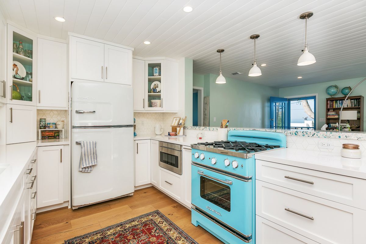 Bright, airy kitchen with turquoise retro stove, white cabinets, and wood floors. Open to a living area with blue accents.