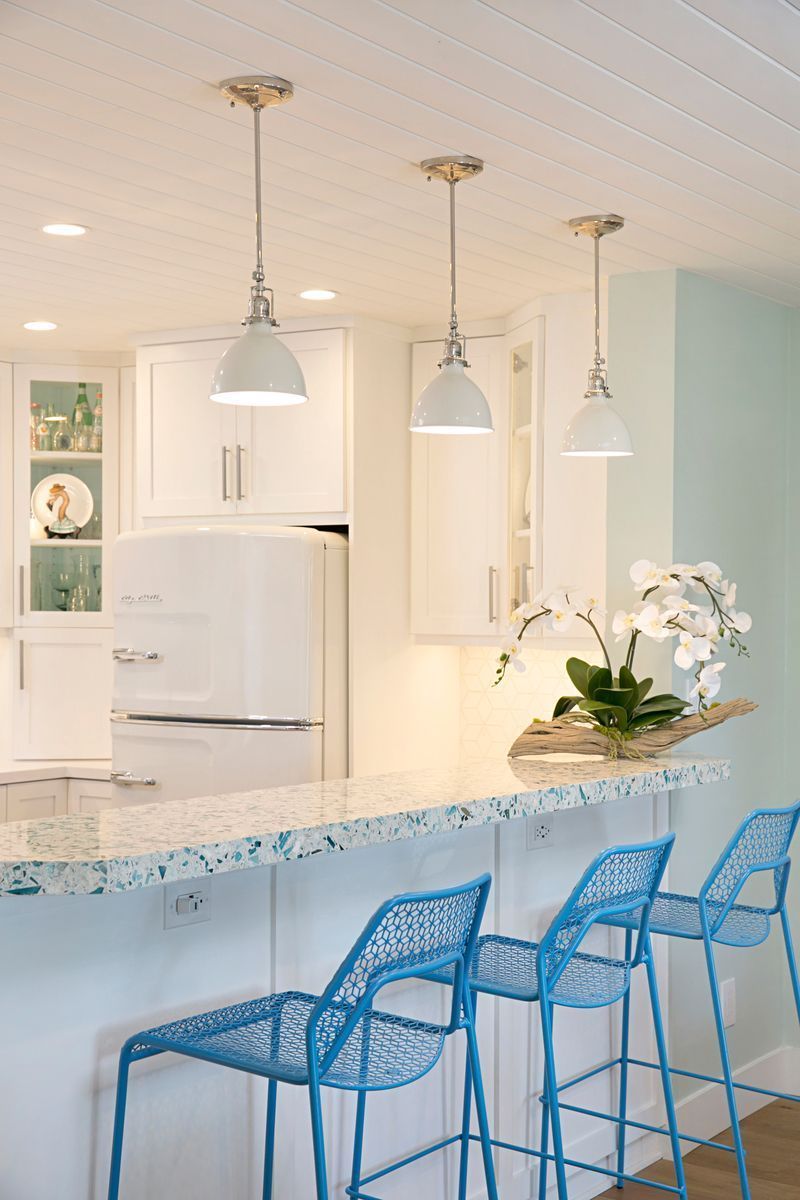Kitchen with white cabinets, blue-topped island, and blue metal bar stools. Three white pendant lights hang above the island.