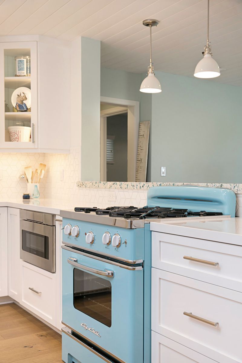 A bright blue retro oven in a white kitchen with pendant lights and a light blue wall in the background.
