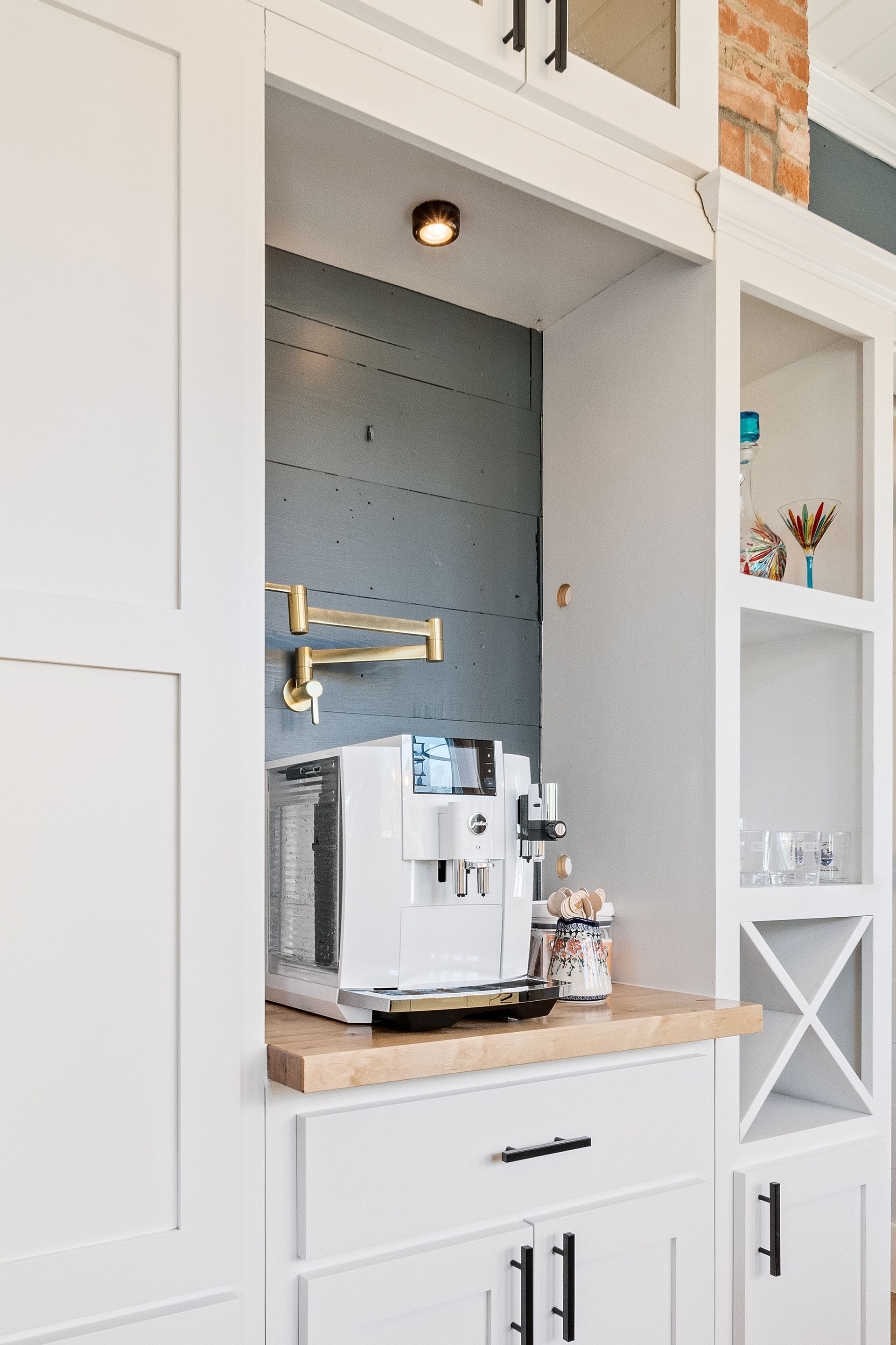 A built-in coffee station with a white espresso machine, gold faucet, and shelves within a white cabinet, a section of blue wall.