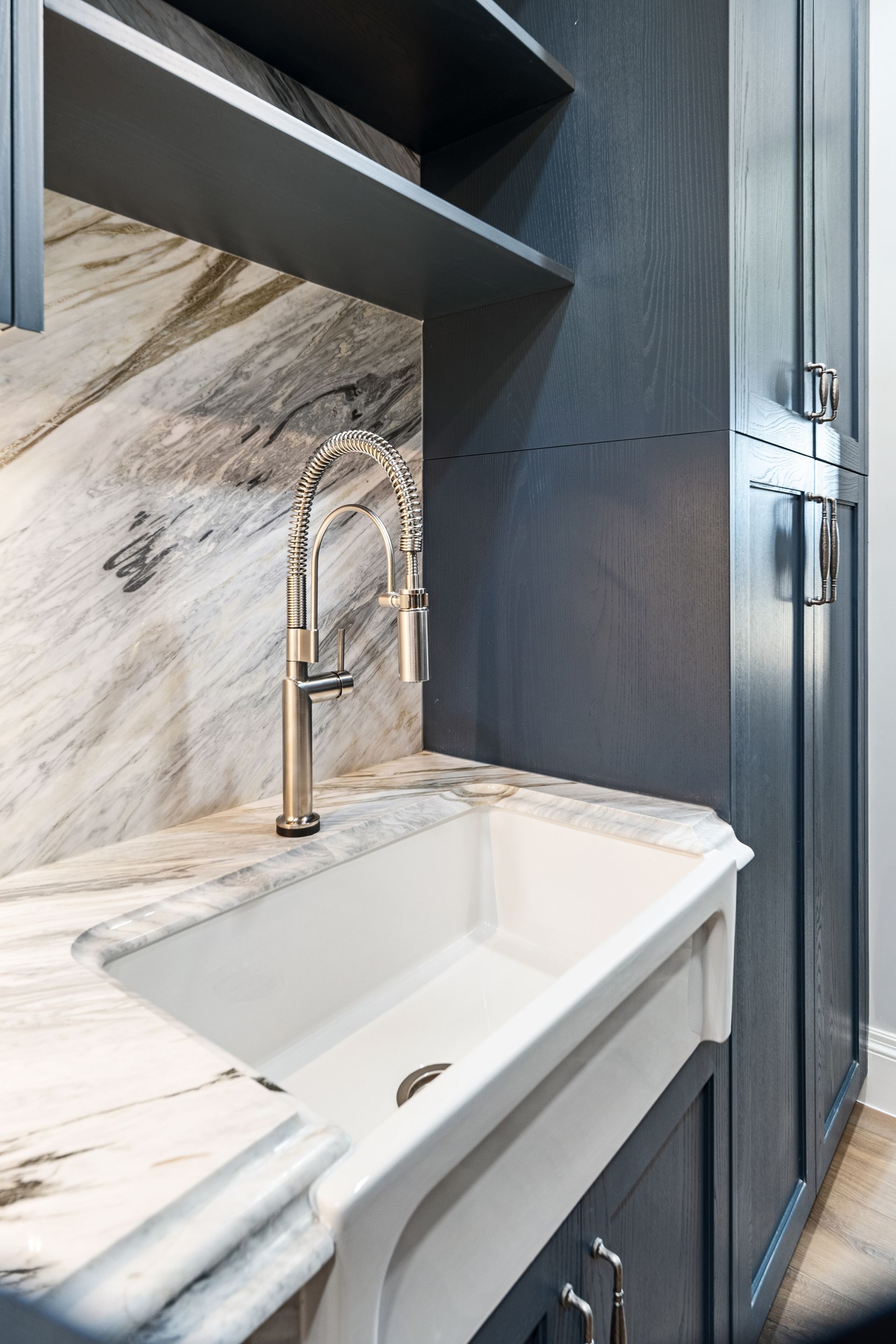 A modern kitchen sink with a pull-down faucet sits against marble-like backsplash and dark cabinetry.