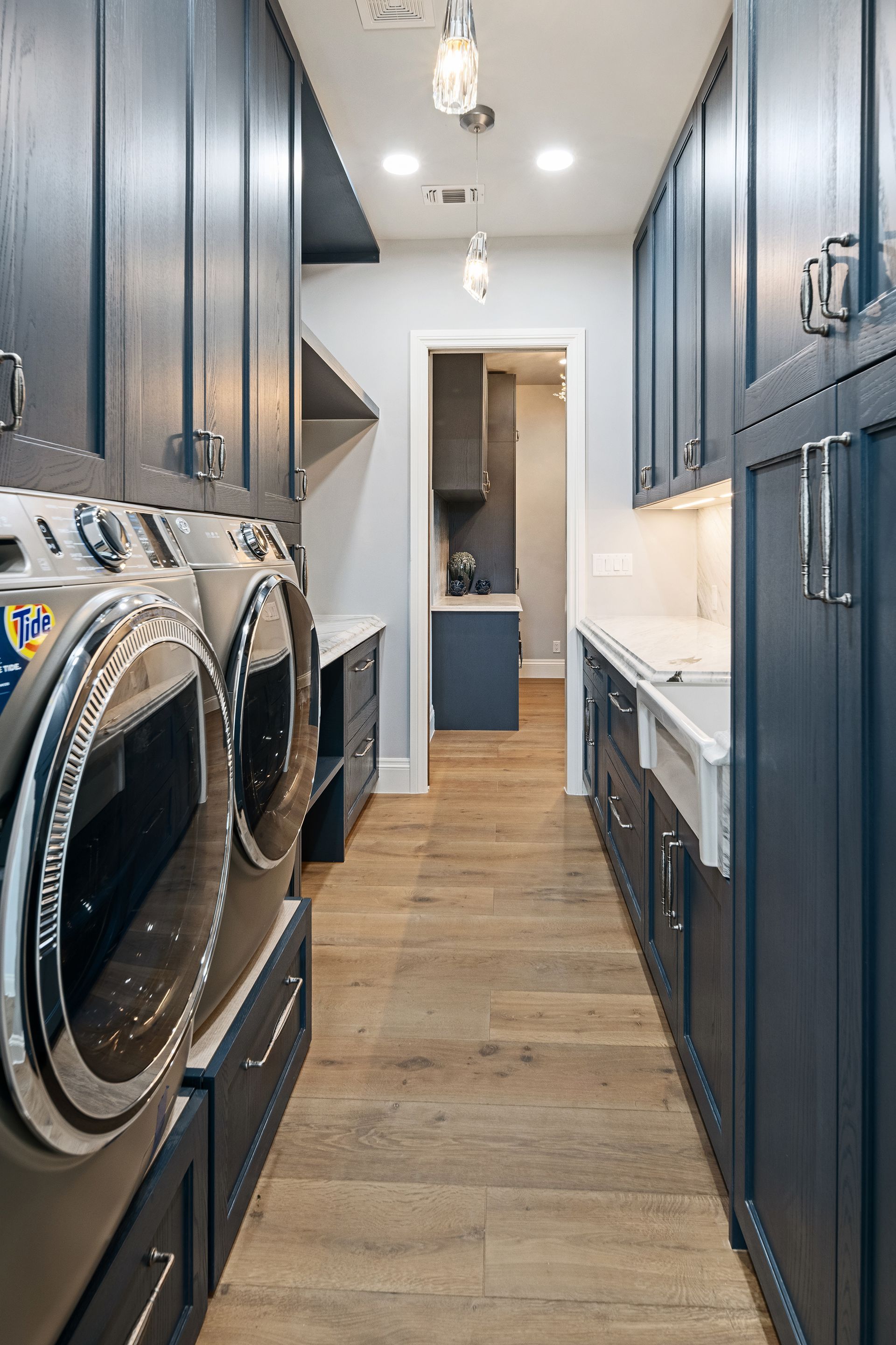 A laundry room with navy blue cabinets and wood flooring. The room has a washer and dryer, countertops, and a doorway to another space.
