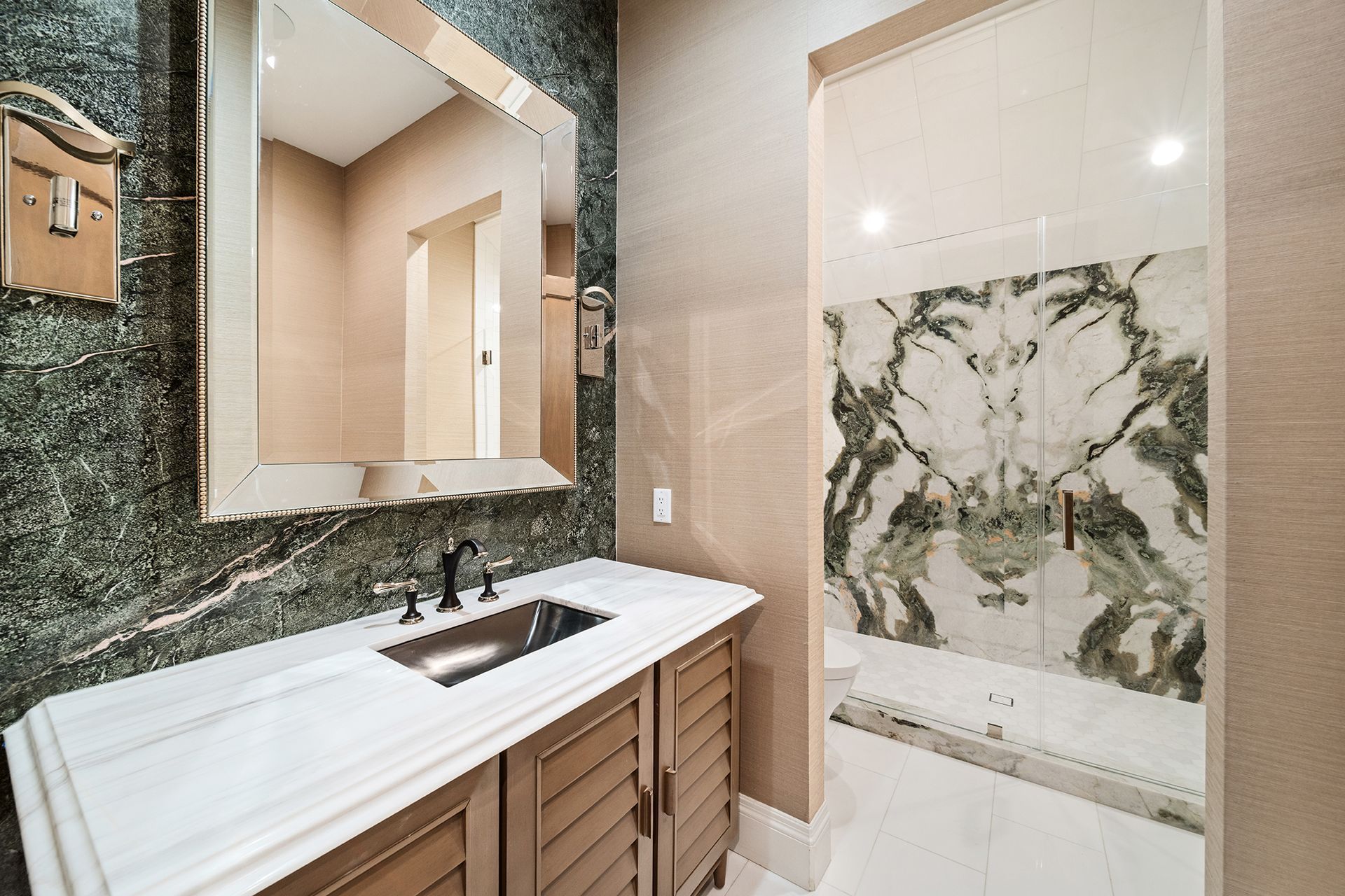 Bathroom with a marble countertop, vanity, and a large mirror. Green marble accent wall, and a patterned glass door leads to another area.