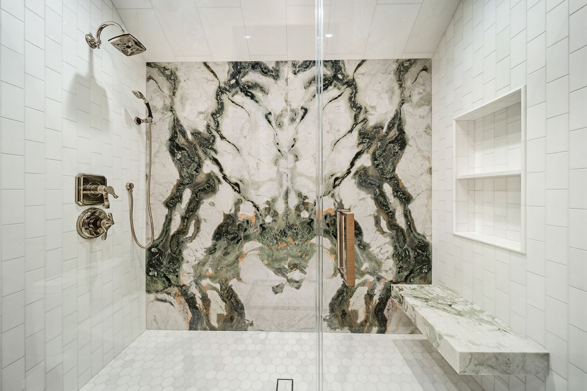Luxurious shower with a large marble slab back wall with green veining, glass door, and built-in bench.