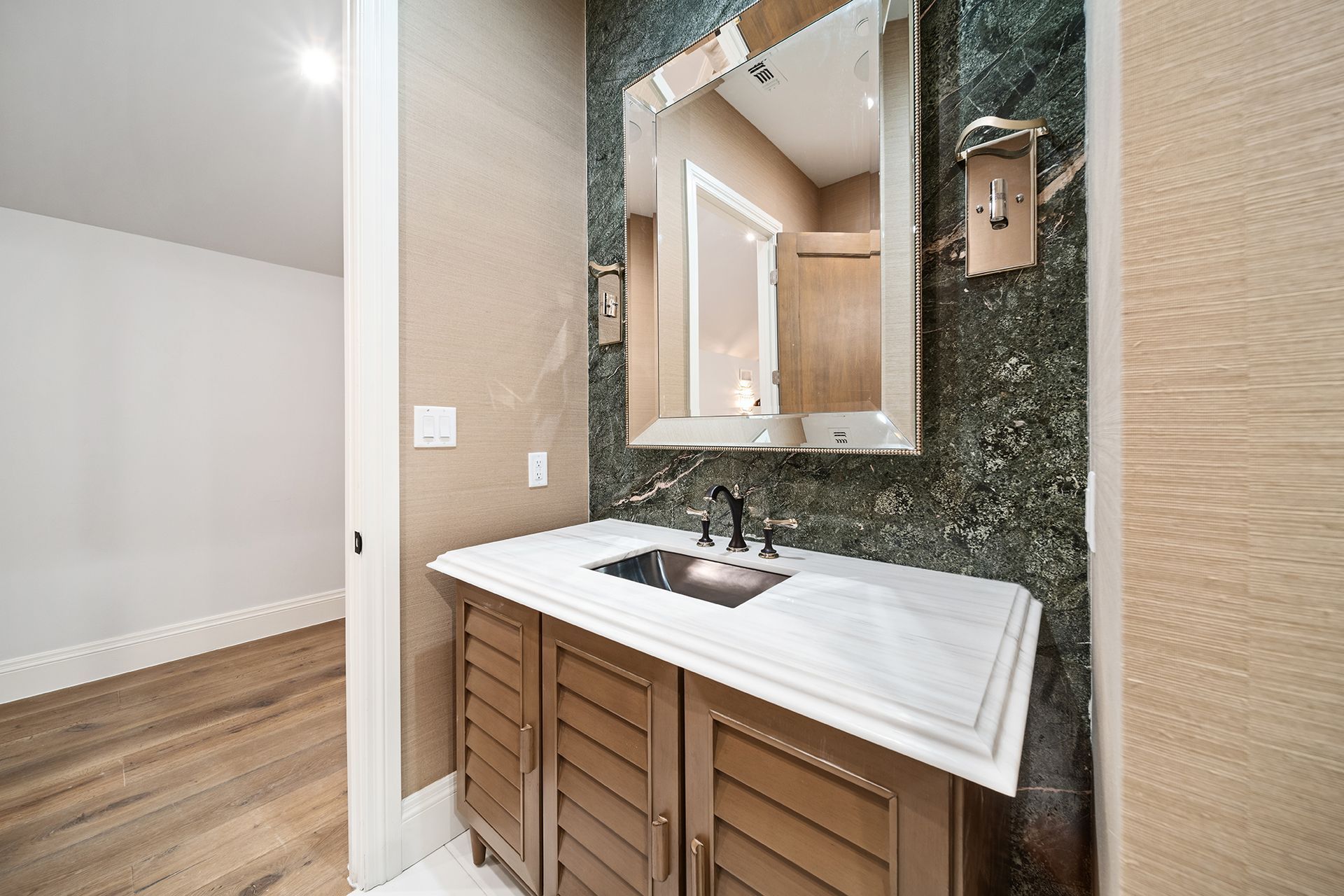 Powder room with a wooden vanity, marble countertop, and a green tiled wall. A large mirror hangs above the sink.