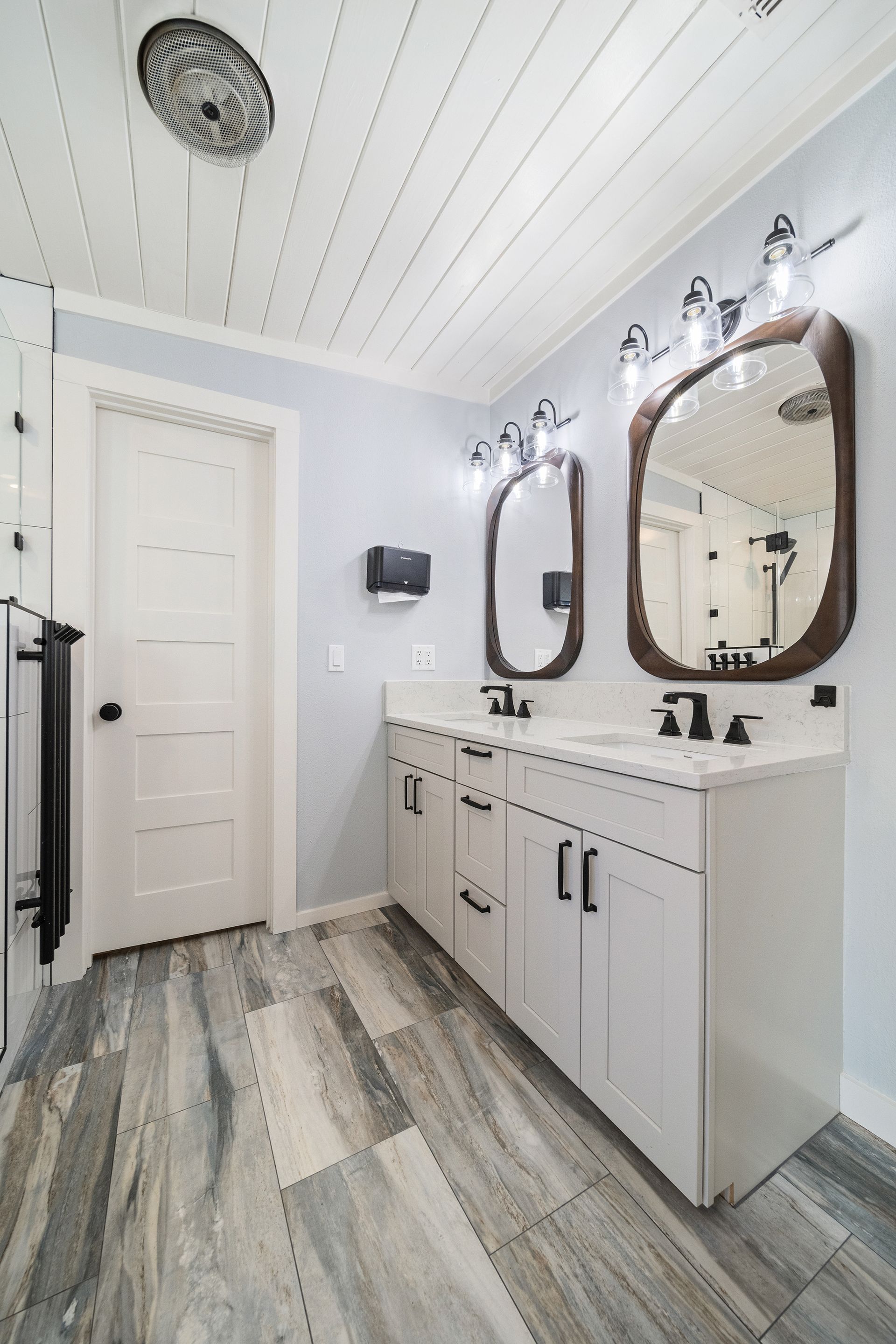 Bathroom with a white double vanity, oval mirrors, and blue walls and wood-look floor.