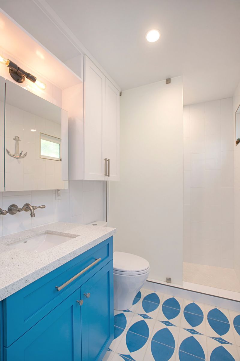 Blue and white nautical-themed bathroom with blue vanity, oval patterned floor tiles, and a glass shower door.