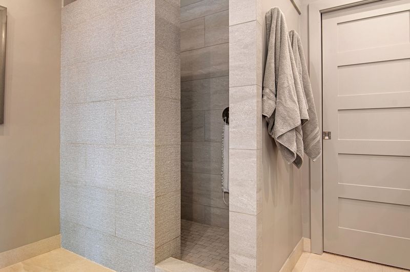 Modern bathroom with a walk-in shower, neutral gray tiles, a towel hanging on the wall, and a closed door.