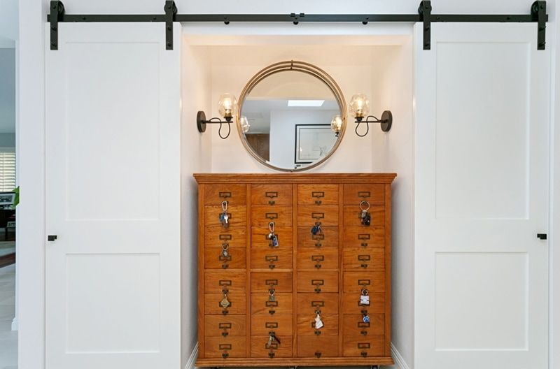 A wooden cabinet with drawers sits beneath a circular mirror, flanked by sconces and white sliding barn doors.
