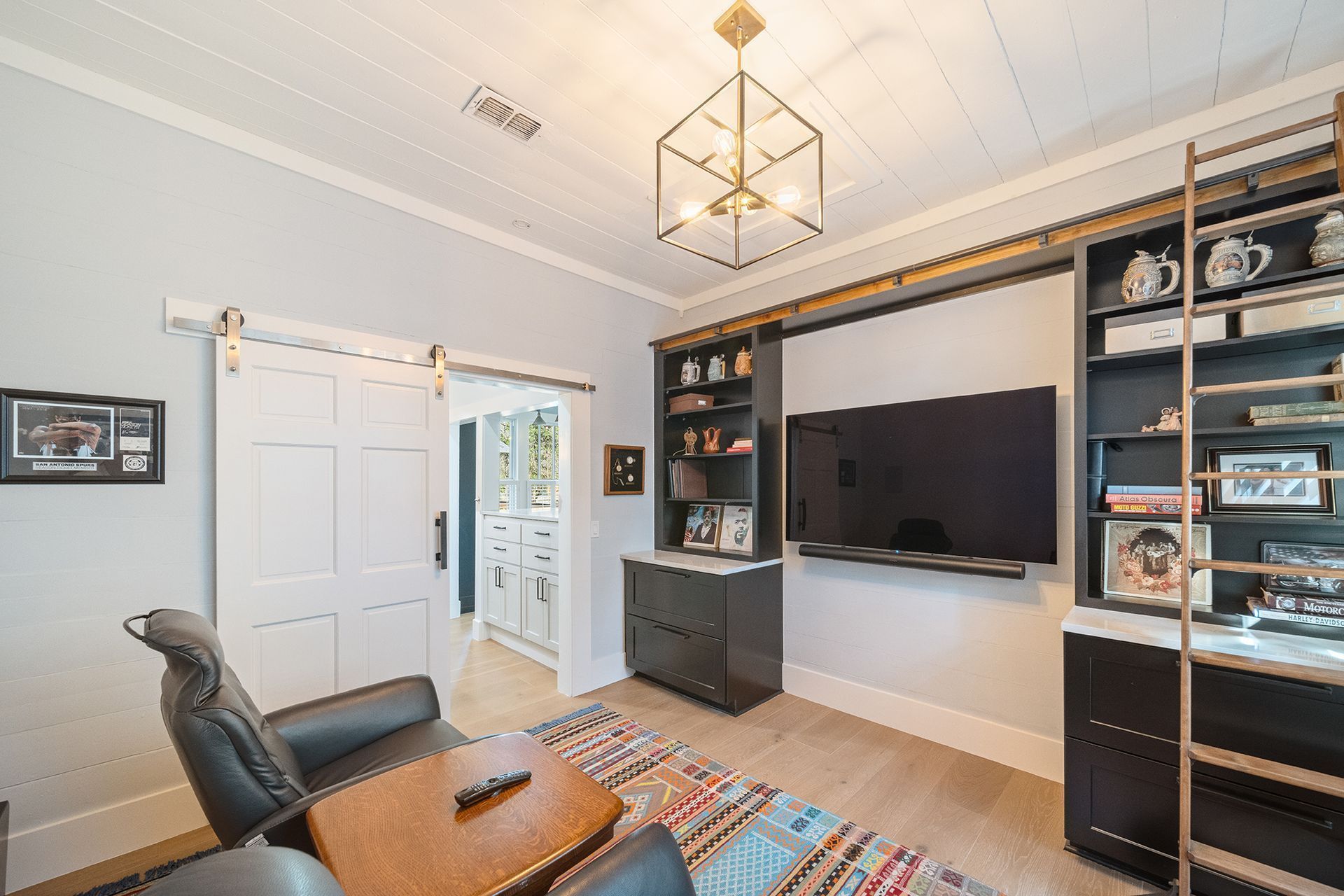Home office with white sliding door, built-in bookshelves, large TV, a leather chair, and a rug.