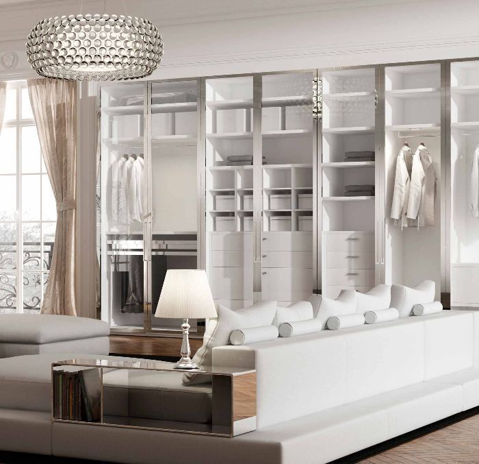 Luxurious white bedroom with large closet and built-in seating. The room is bright, with a large window and chandelier.