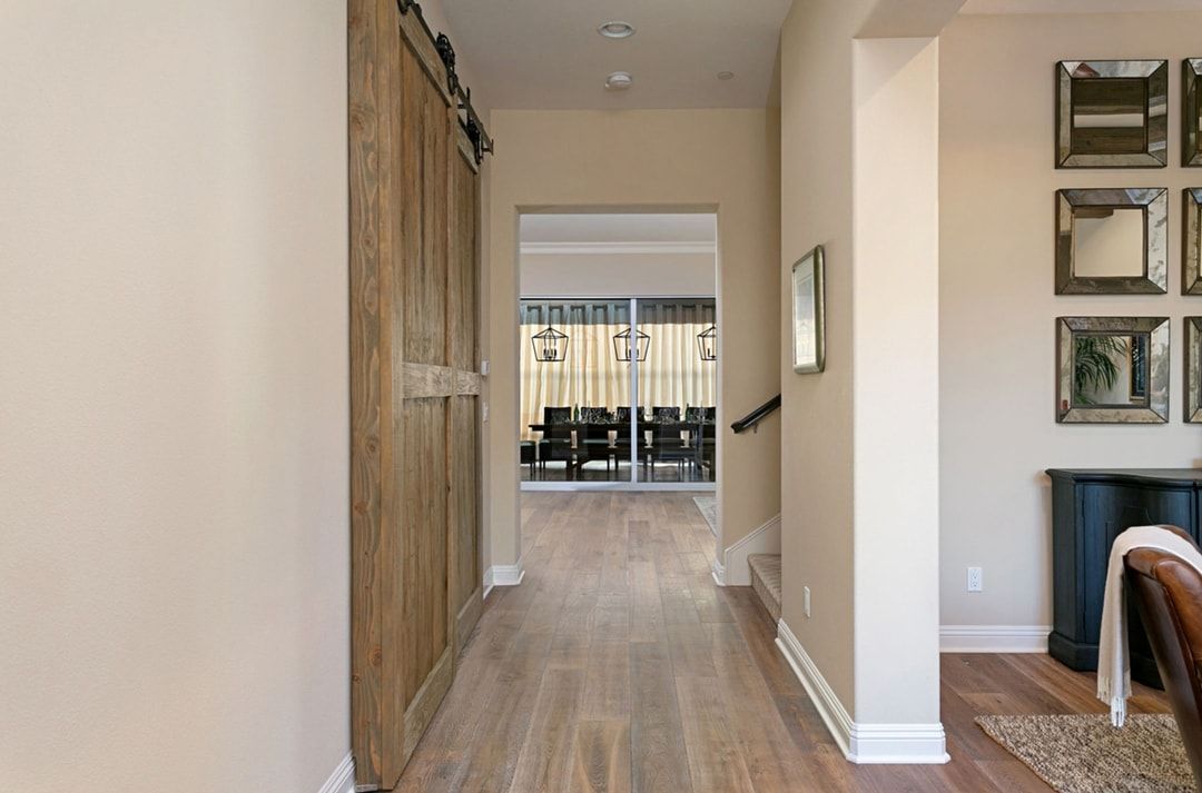 Hallway with wooden floor and a view to a dining area through an opening. A large wooden cabinet is on the left.