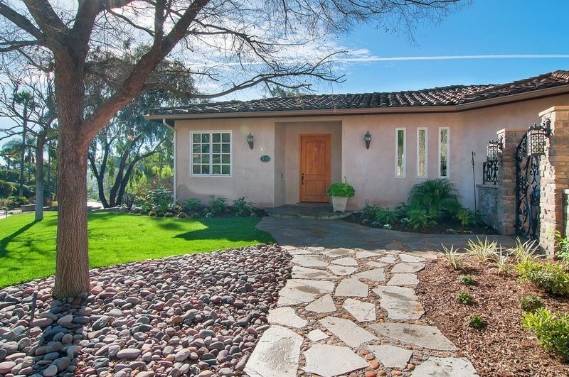A house with a stone walkway and a brown wooden door, under a bright blue sky.