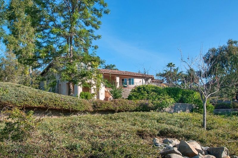 A house with a tile roof nestled in greenery under a clear blue sky.