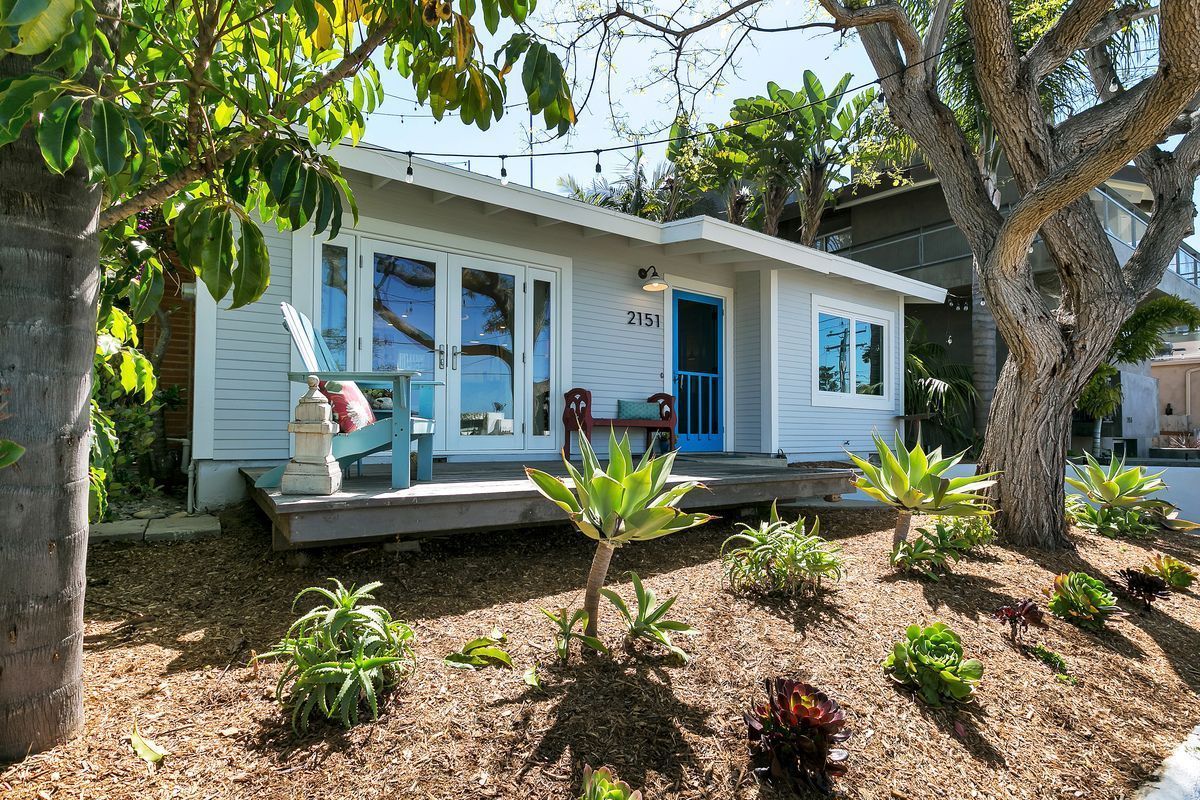 Small, light blue beach house with a blue door and front porch. Exterior features include landscaping and trees.