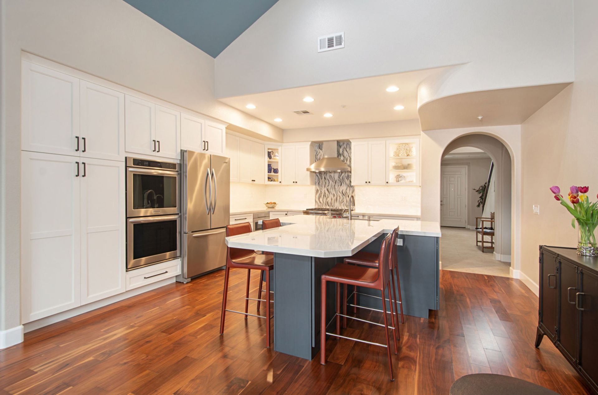 A kitchen with white cabinets , stainless steel appliances , hardwood floors and a large island.