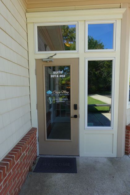 Glass front door with sidelight and transom, tan trim, brick base, and a doormat on a small porch