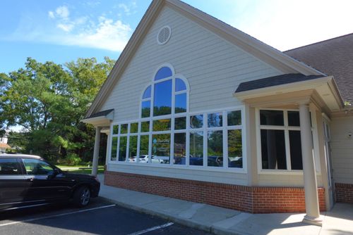 Front of a beige building with large arched windows, brick base, and a parked black car.