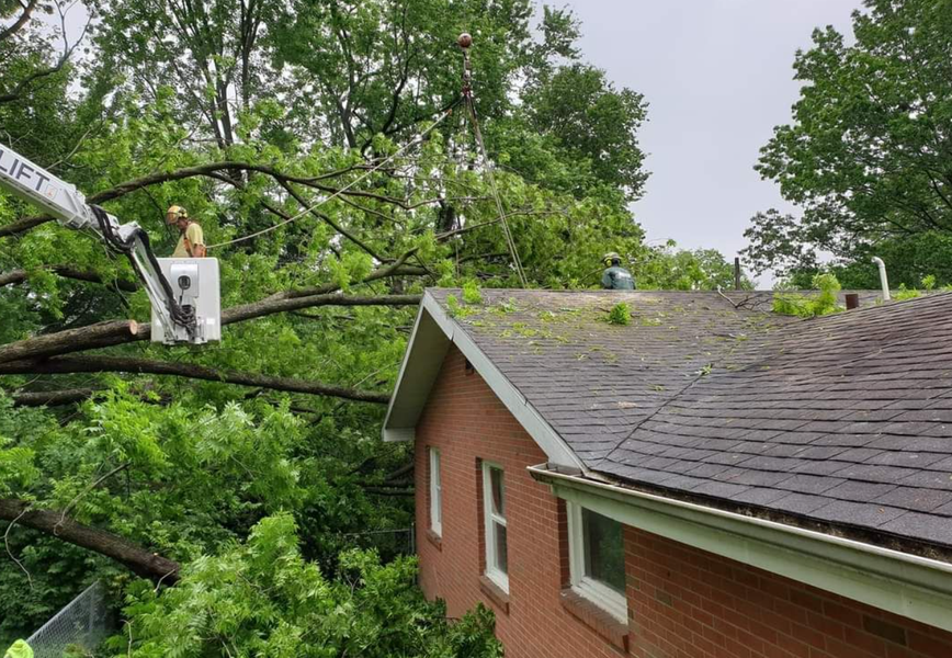 Tree service workers trimming branches off of a house roof, using a lift.