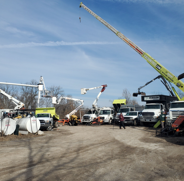 A lot of utility trucks and cranes in a yard on a sunny day.