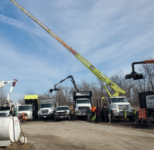 Trucks, equipment, and a work crew outdoors on a sunny day, presumably for tree removal or related services.