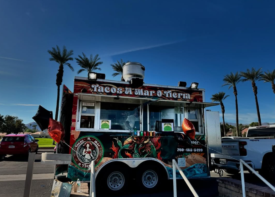 A taco truck is parked in a parking lot with palm trees in the background