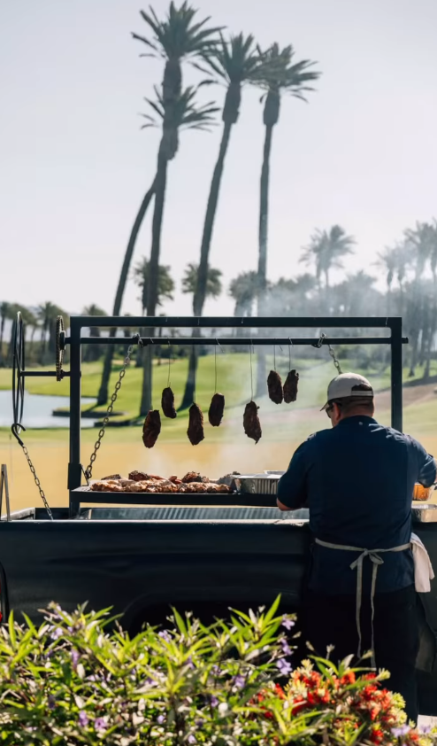 A man standing in front of a grill with palm trees in the background