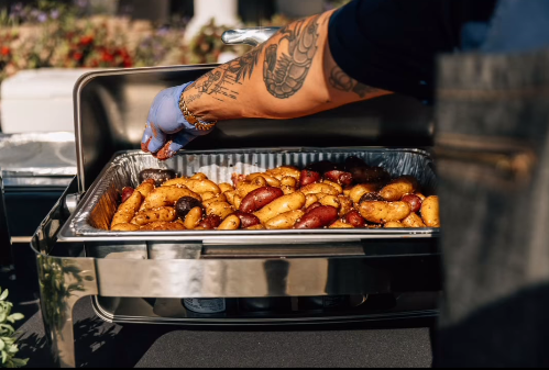A person is taking food out of a buffet tray.