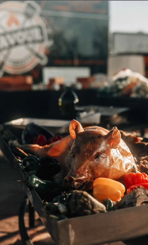 A pig 's head is sitting on top of a wooden tray filled with vegetables.