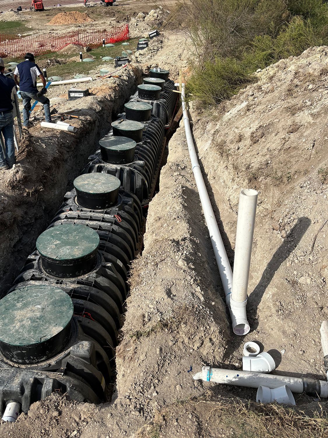 A trench construction site with a line of black plastic septic chambers alongside a white PVC pipe.