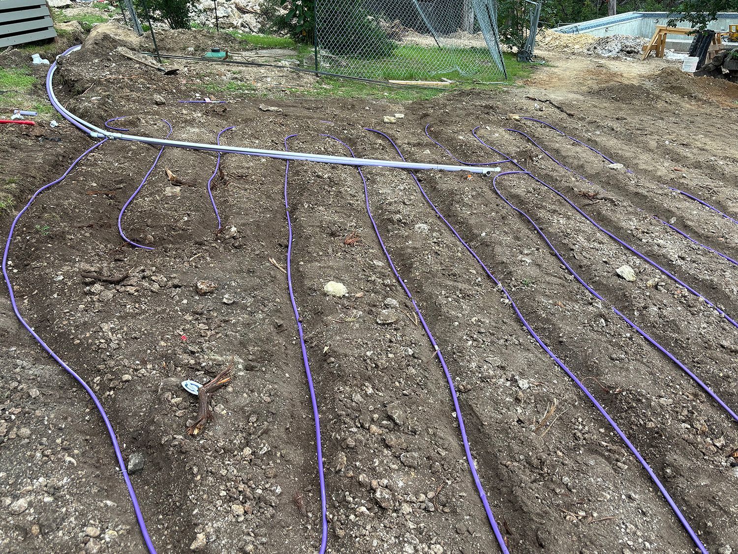 Purple irrigation tubing laid in rows across a tilled garden bed in an outdoor setting.